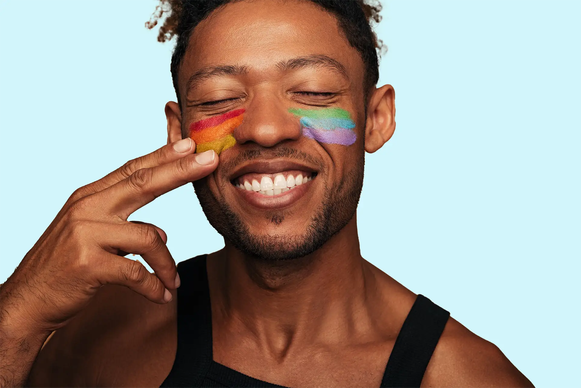 Man smiling with eyes closed and putting on rainbow colored makeup